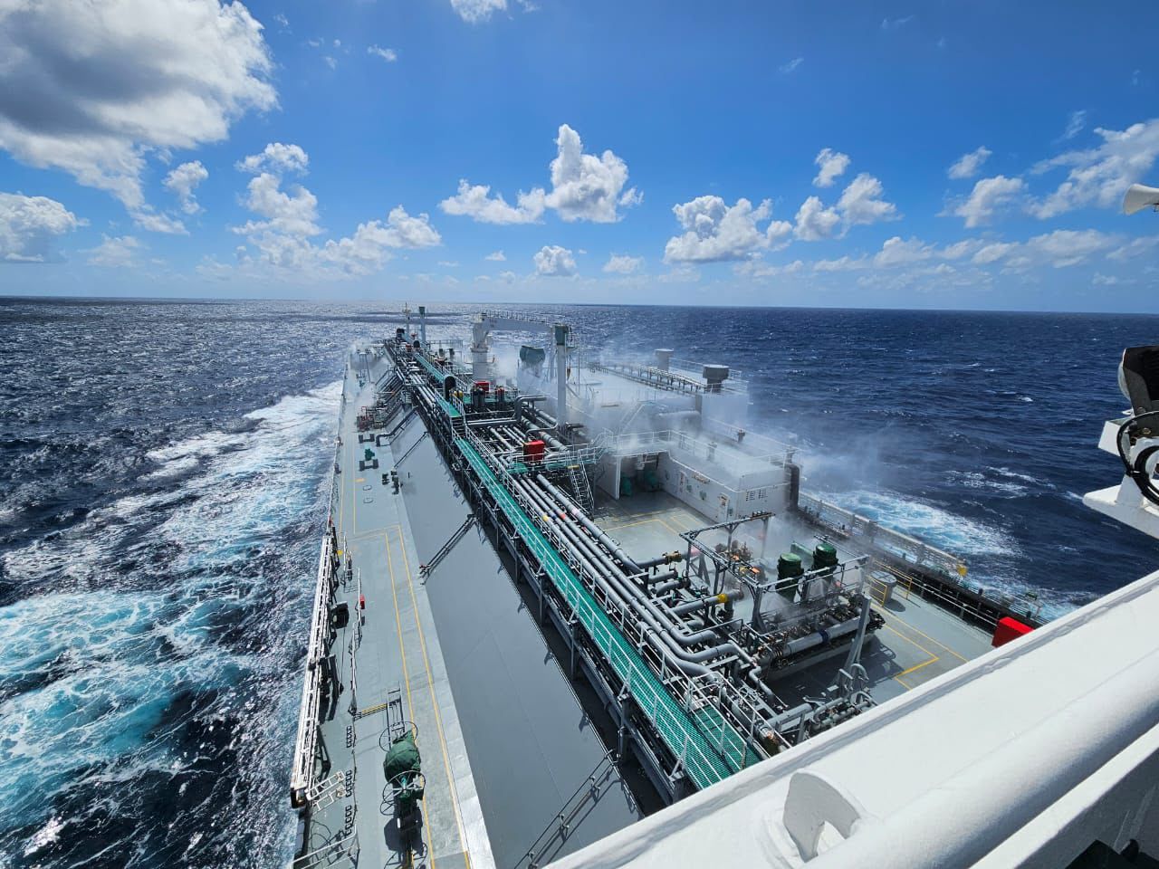 The deck of the ship Uditanshu serves on, crossing open sea under a blue sky